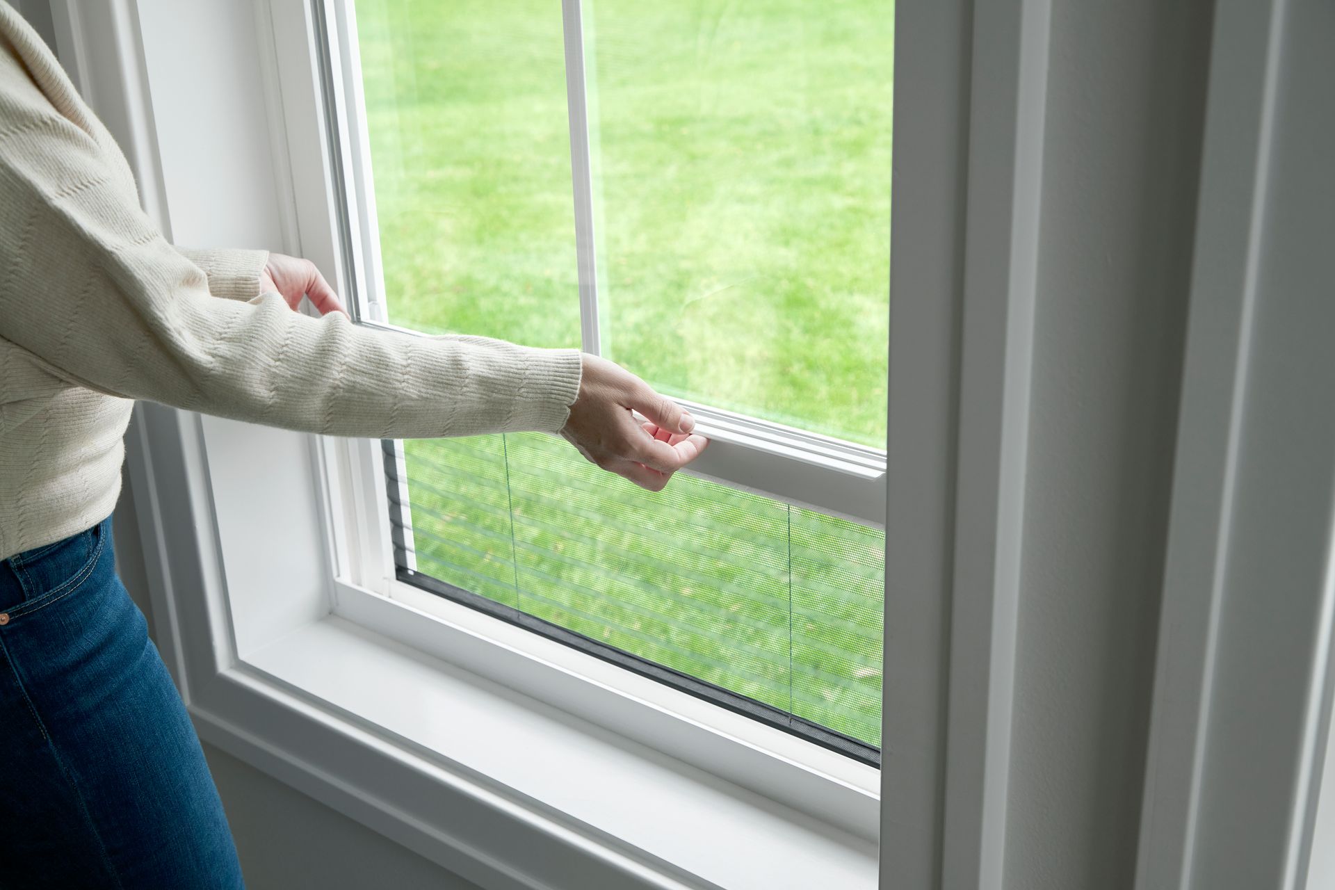 A hand opening a new white Jerco window onto a green lawn